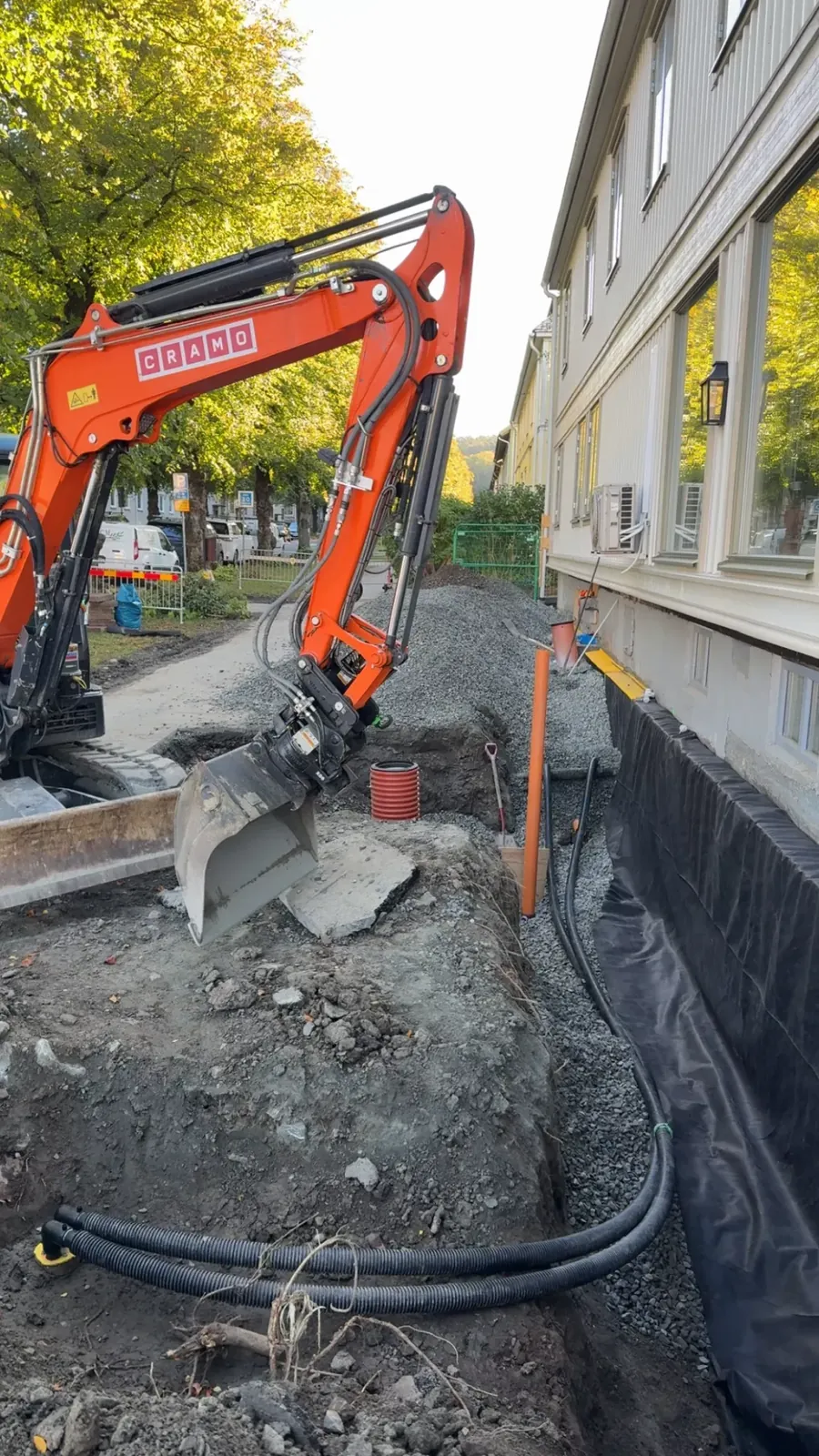 Grävmaskin och dräneringsrör längs ett hus