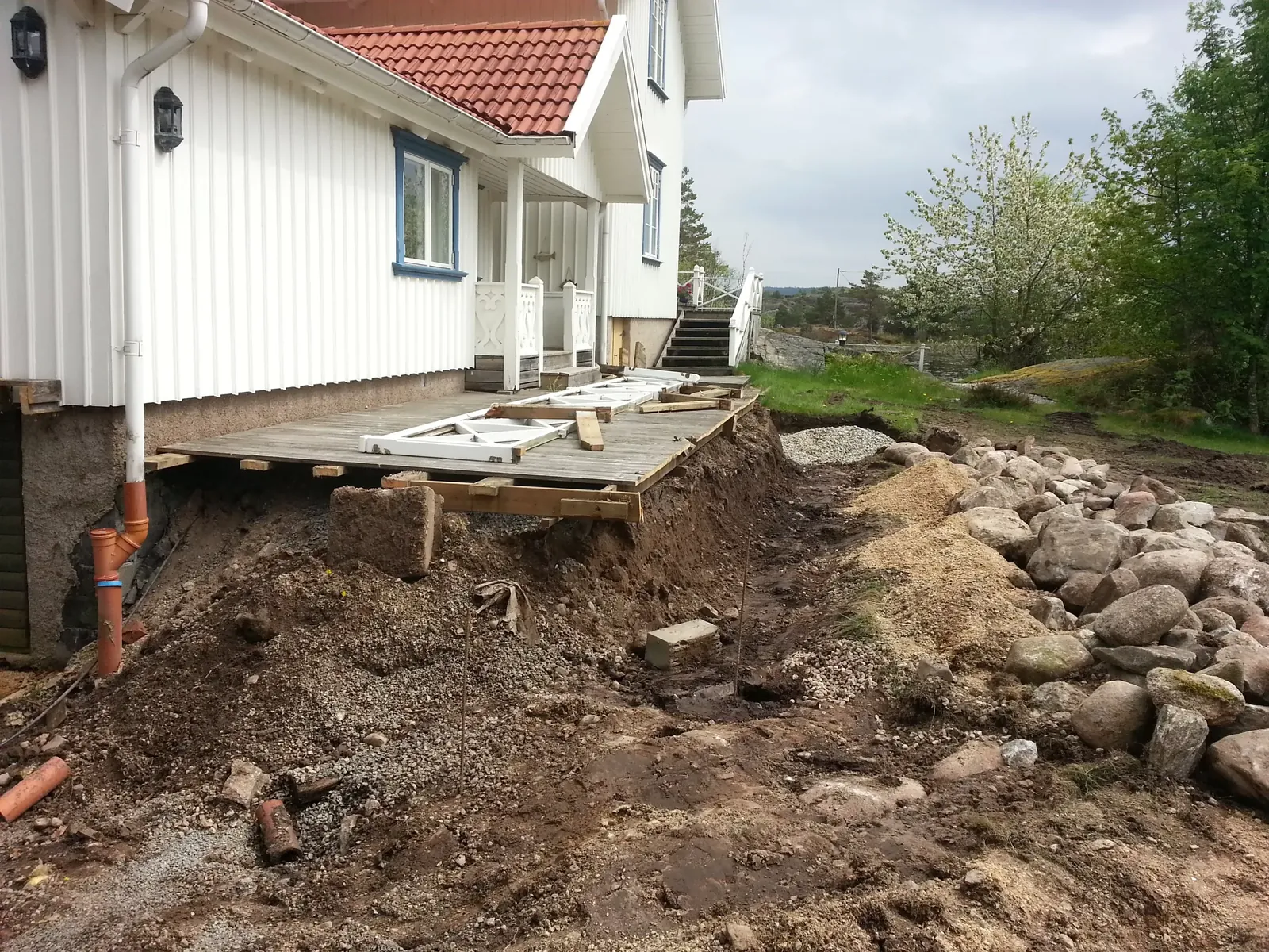 Uppgrävd mark vid ett vitt hus innan stenmuren byggdes