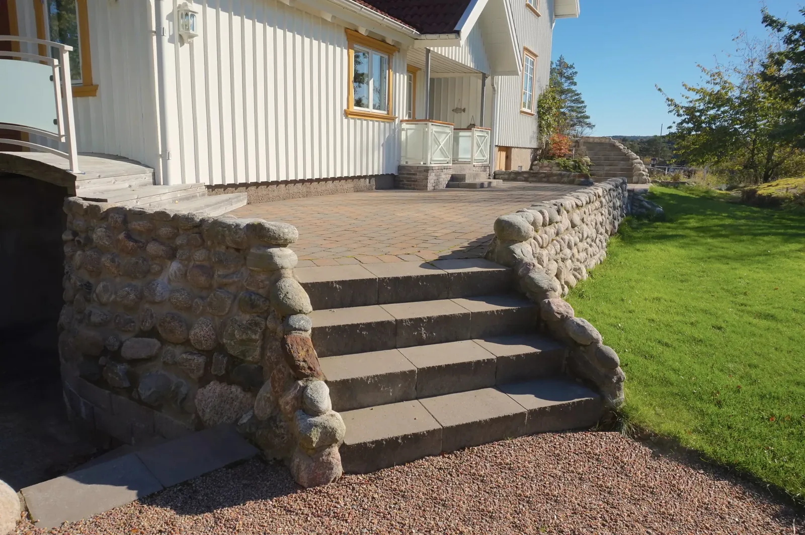 Ny trappa och mur i natursten vid ett vitt hus