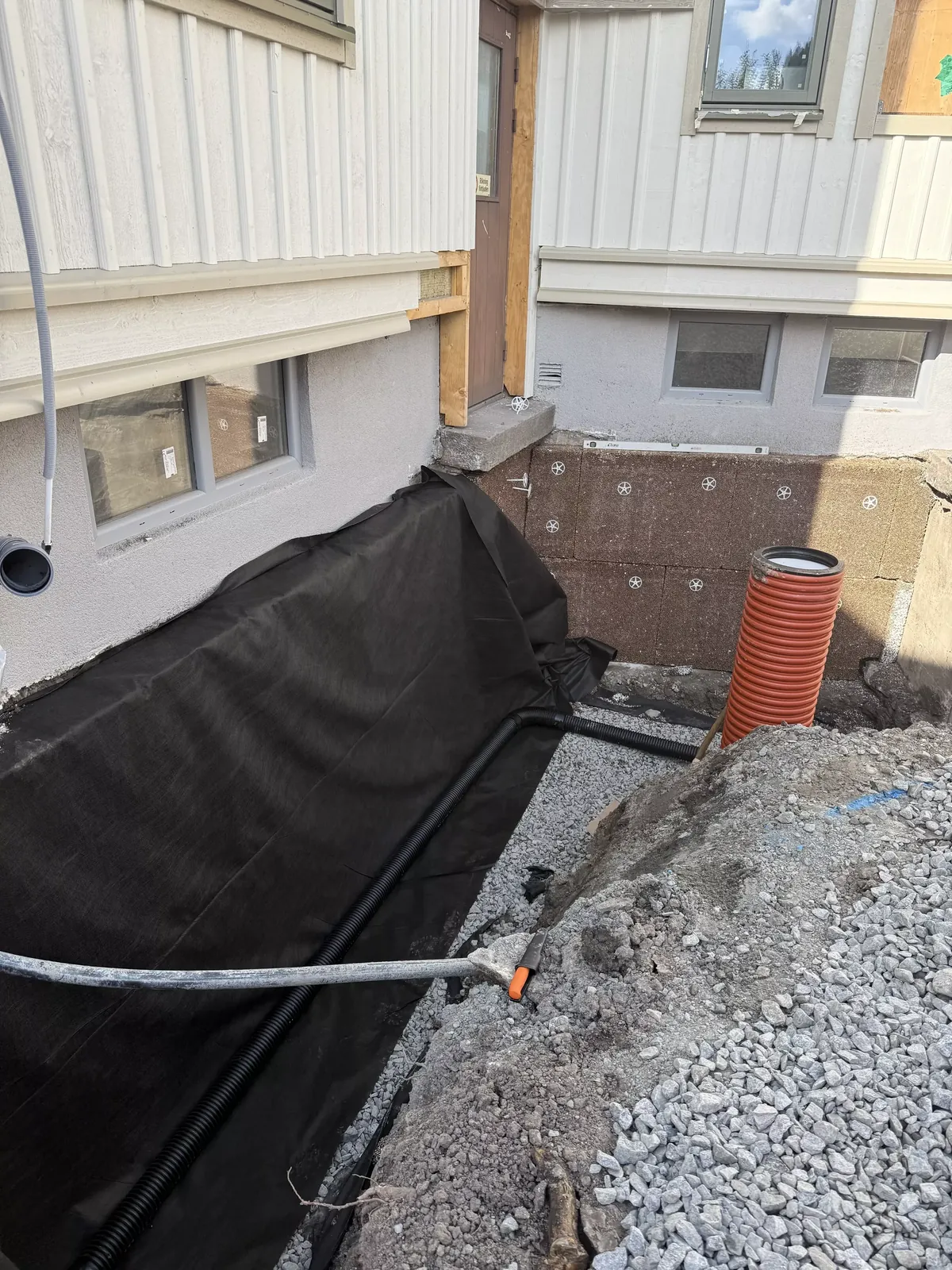 Grundmur med fuktskydd och dräneringsrör vid ett vitt hus