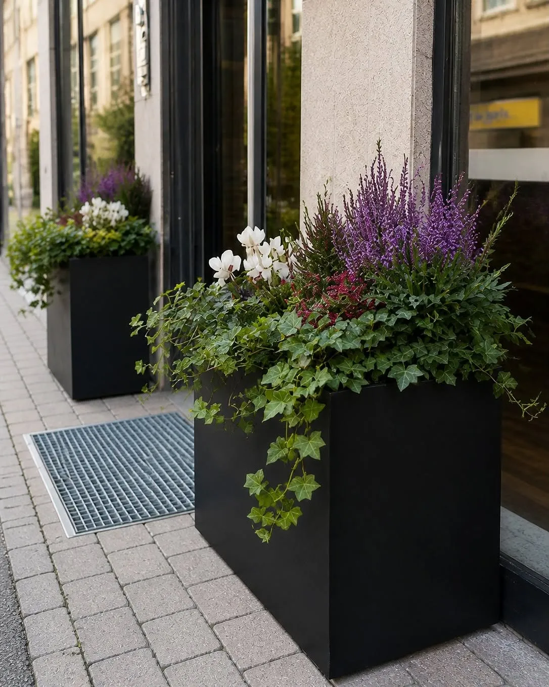 Svarta planteringskärl med blommande växter vid en entré