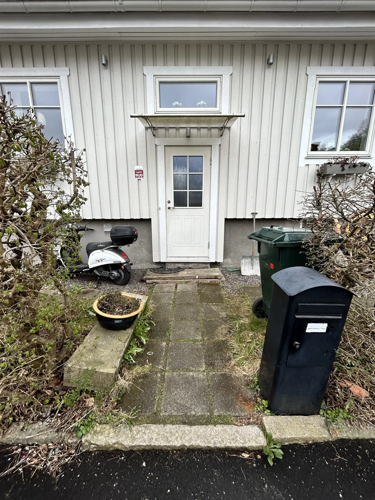 Sliten entré med gamla plattor vid ett vitt trähus
