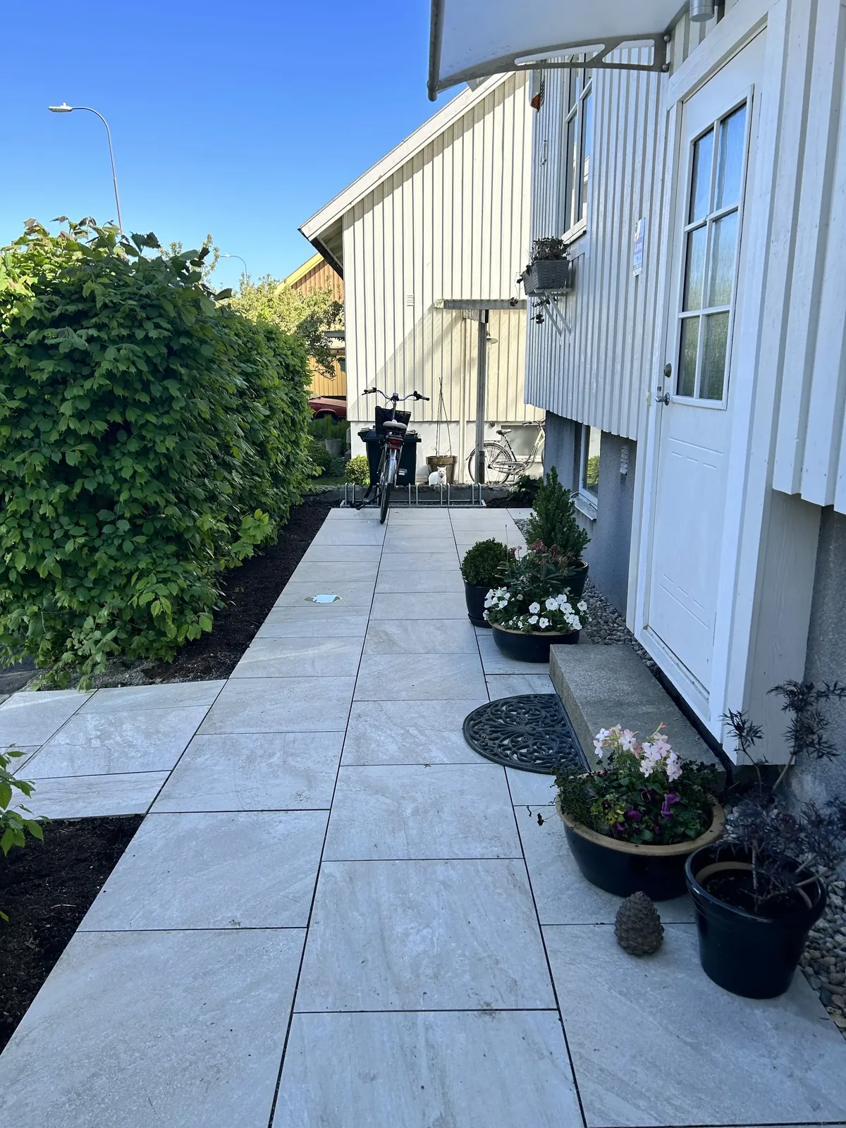 Ny ljus stenläggning längs ett vitt trähus