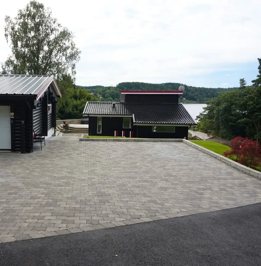 Nylagd stenläggning på en uppfart framför ett svart hus vid vattnet