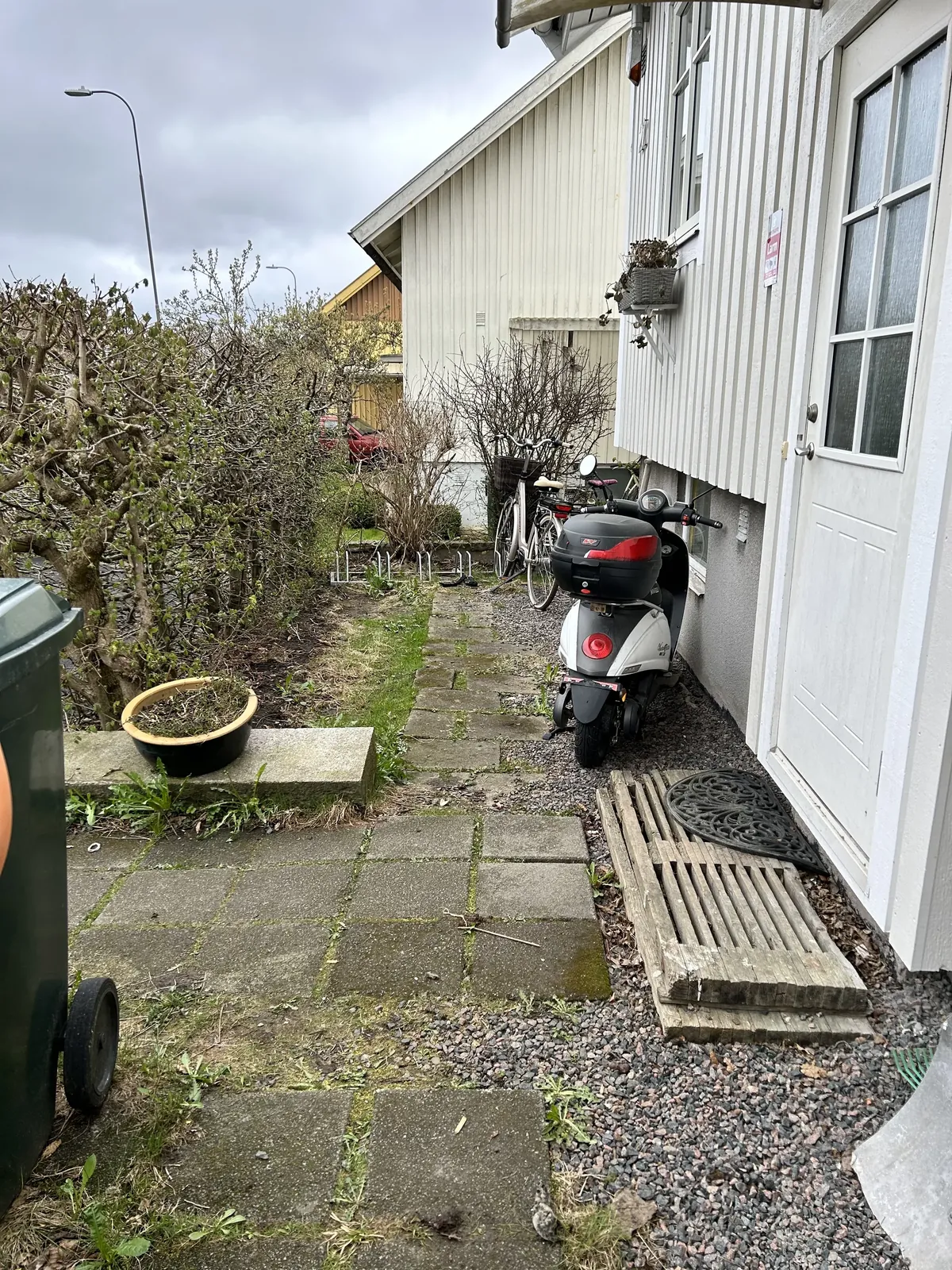 Igenvuxen gång längs ett vitt trähus innan arbetet