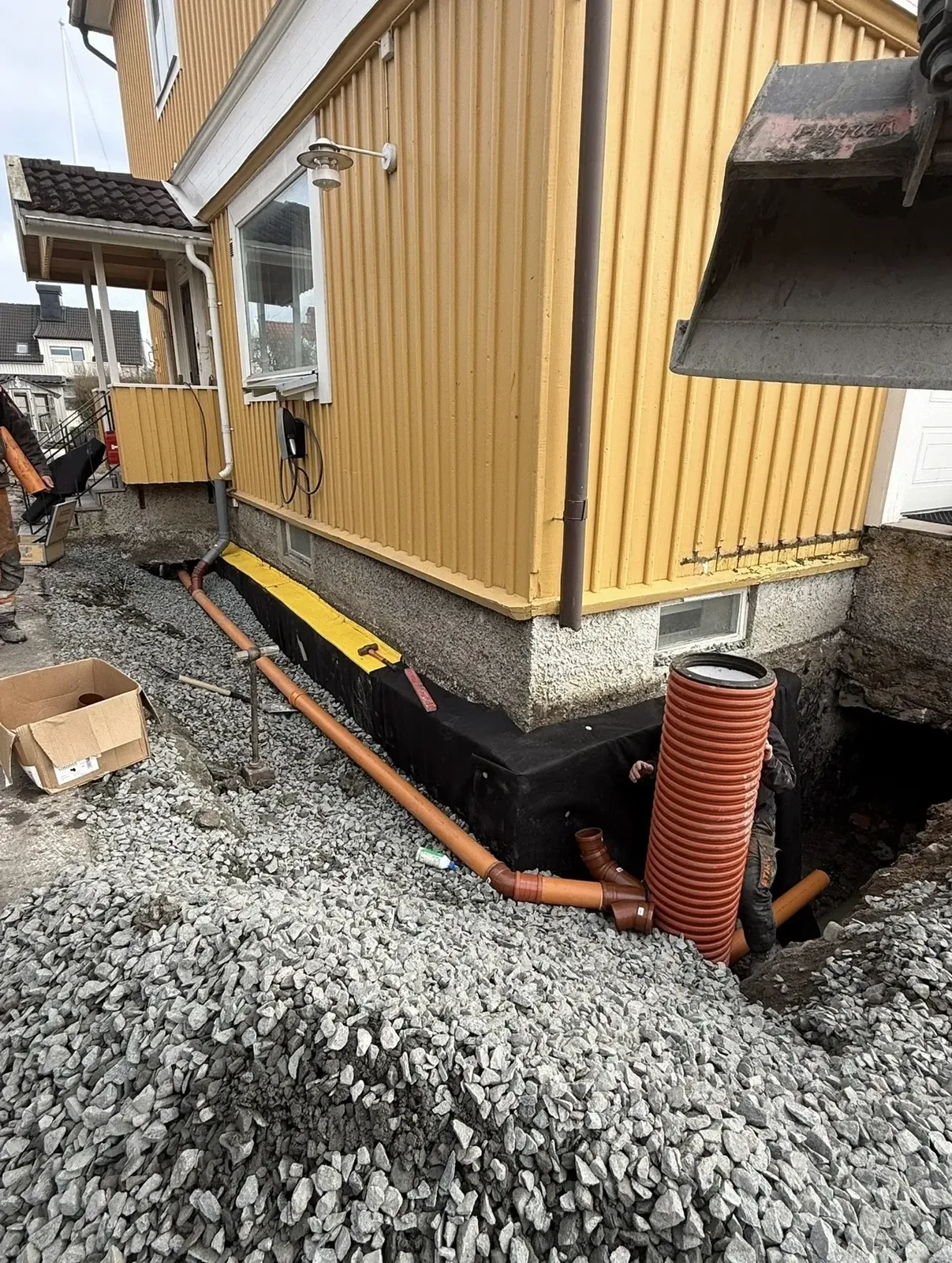 Dräneringsrör och makadam vid husgrunden under arbetet