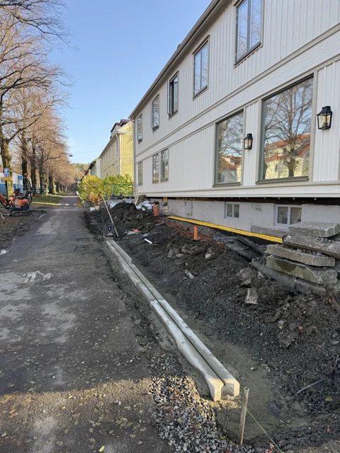 Schaktad mark längs ett ljust trähus under dräneringsarbetet