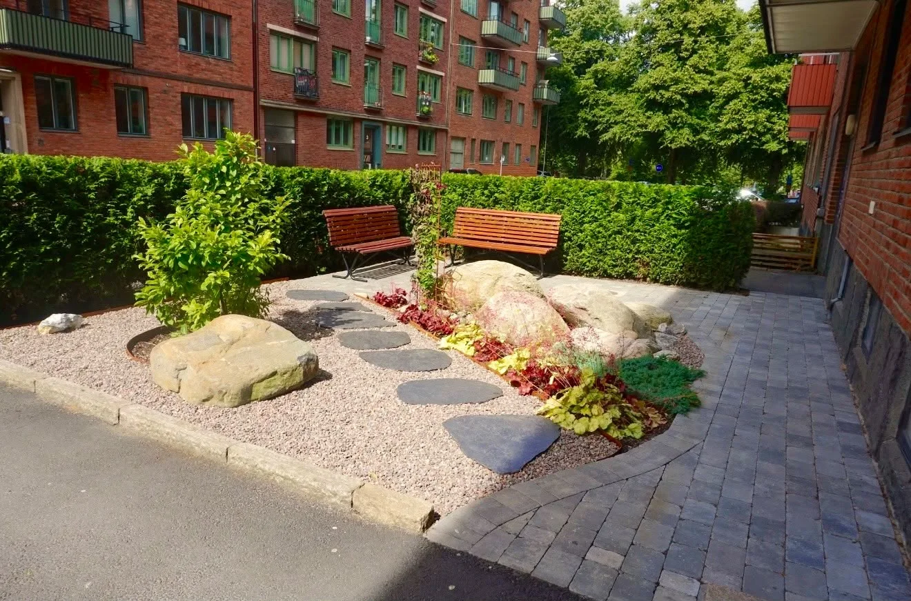 Gräsytan omgjord till en sittplats med stenar, bänkar och planteringar