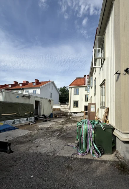 Gårdsplan med grus och material bakom ett ljust trähus under arbetet