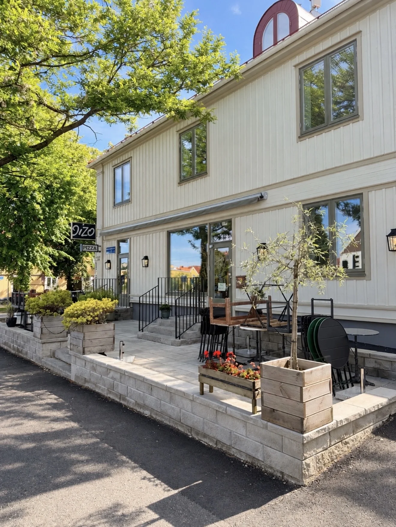 Färdig uteplats med marksten, mur och planteringslådor framför ett ljust trähus