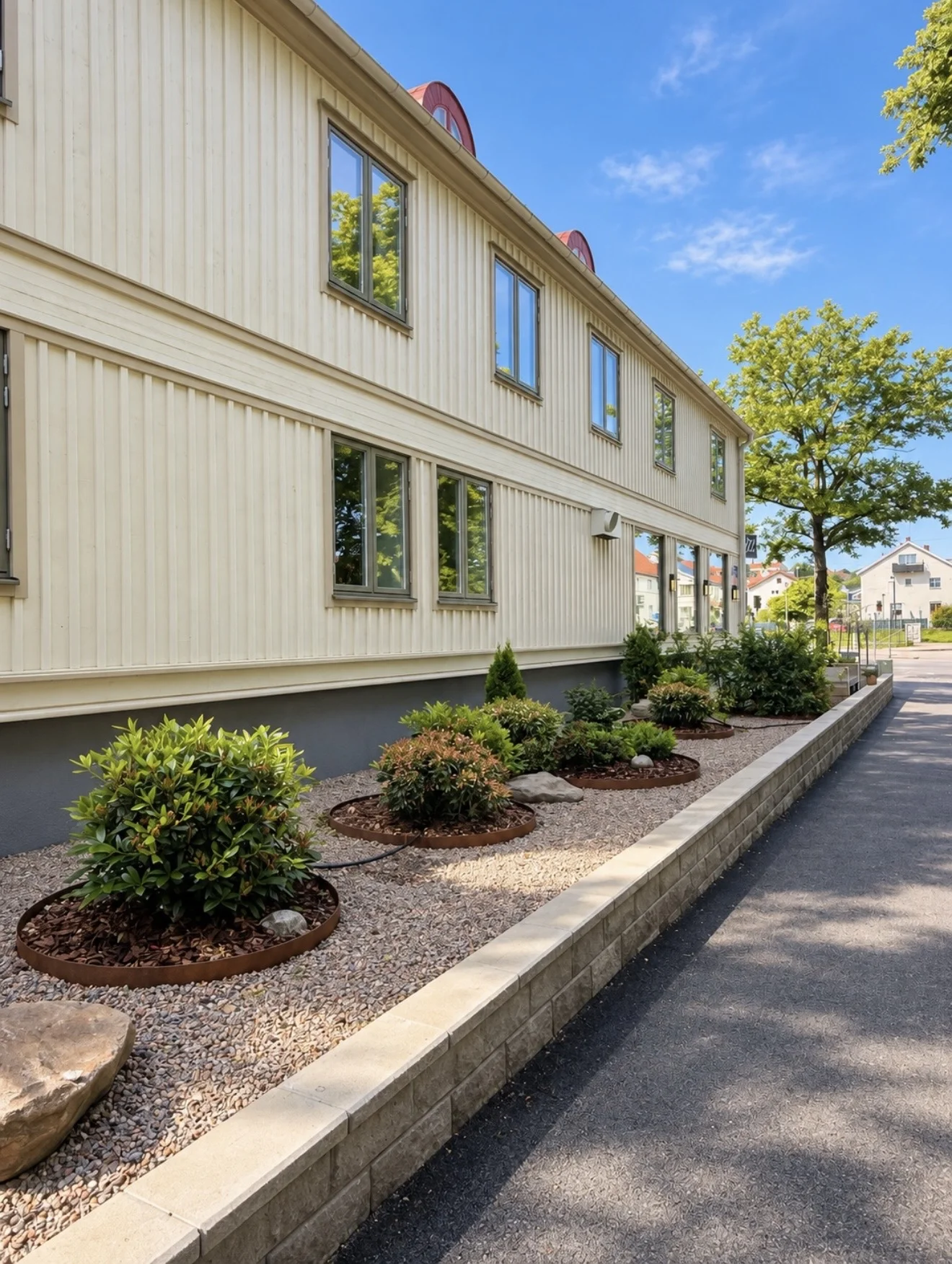 Färdig rabatt med buskar, singel och kantmur längs ett ljust trähus