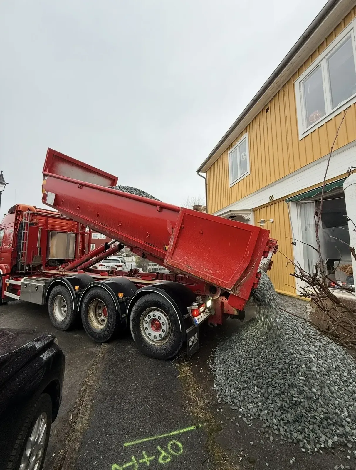 Lastbil tippar makadam vid ett gult hus inför dränering