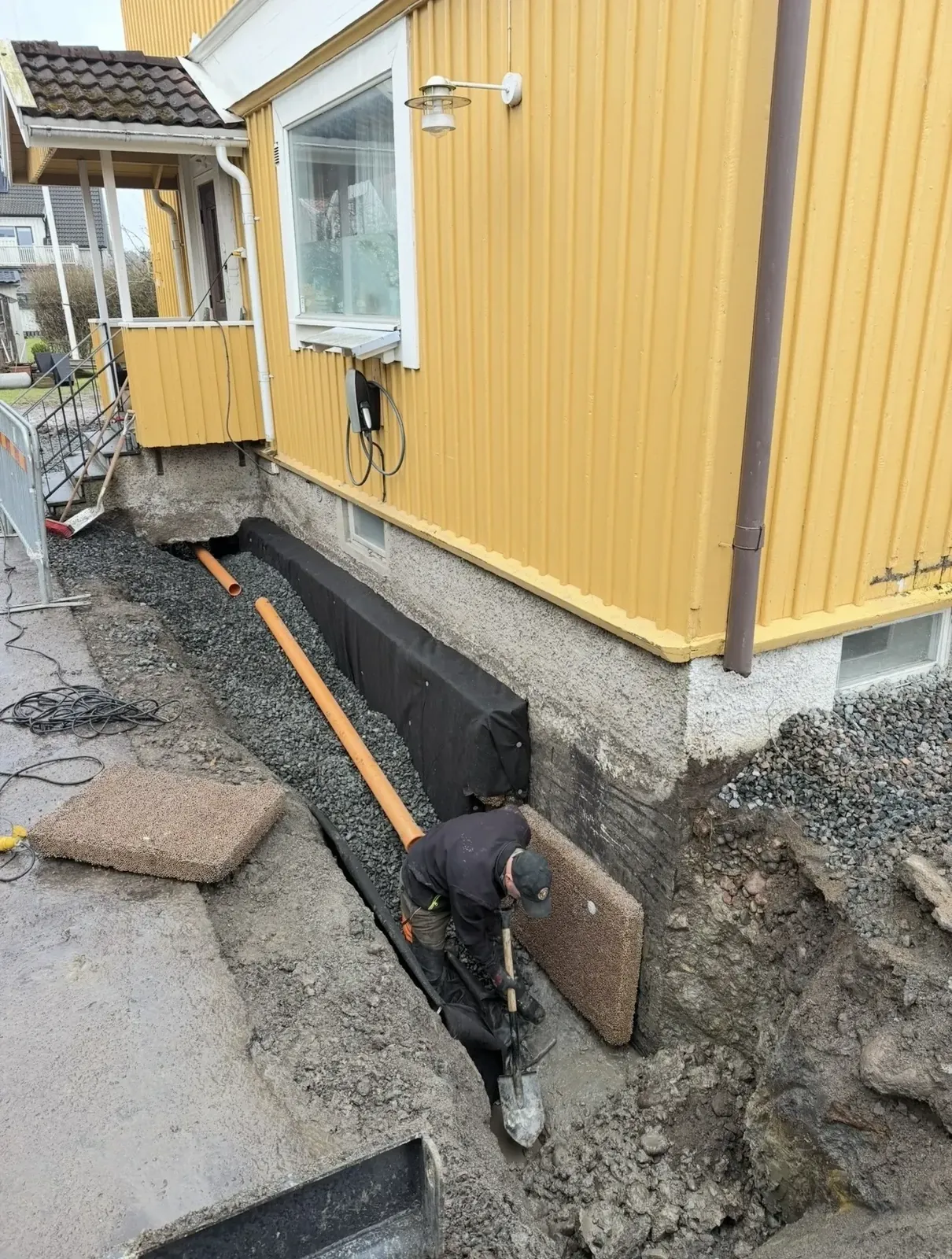 Medarbetare lägger dräneringsrör längs husgrunden