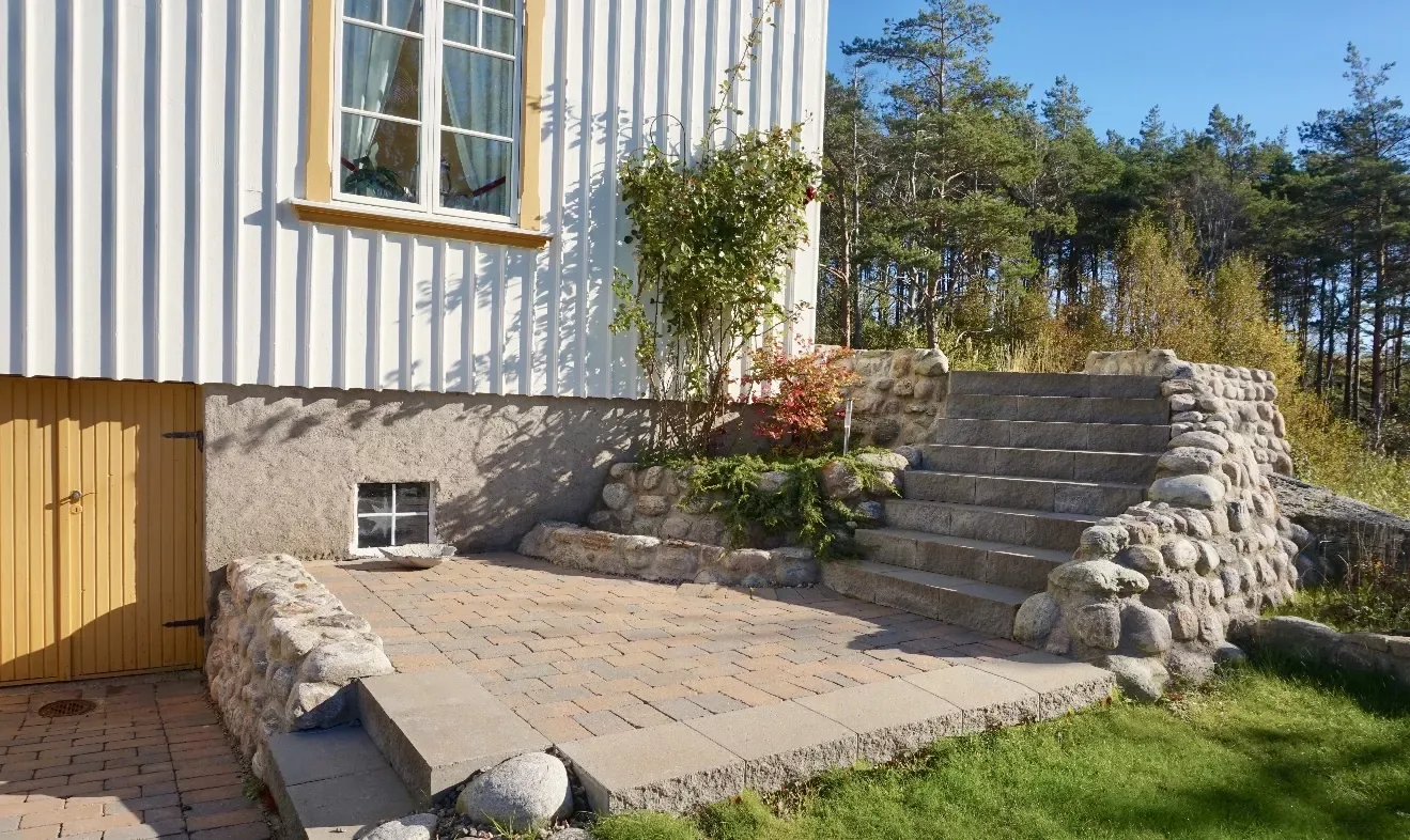 Uteplats och trappa i natursten vid ett hus med gul dörr