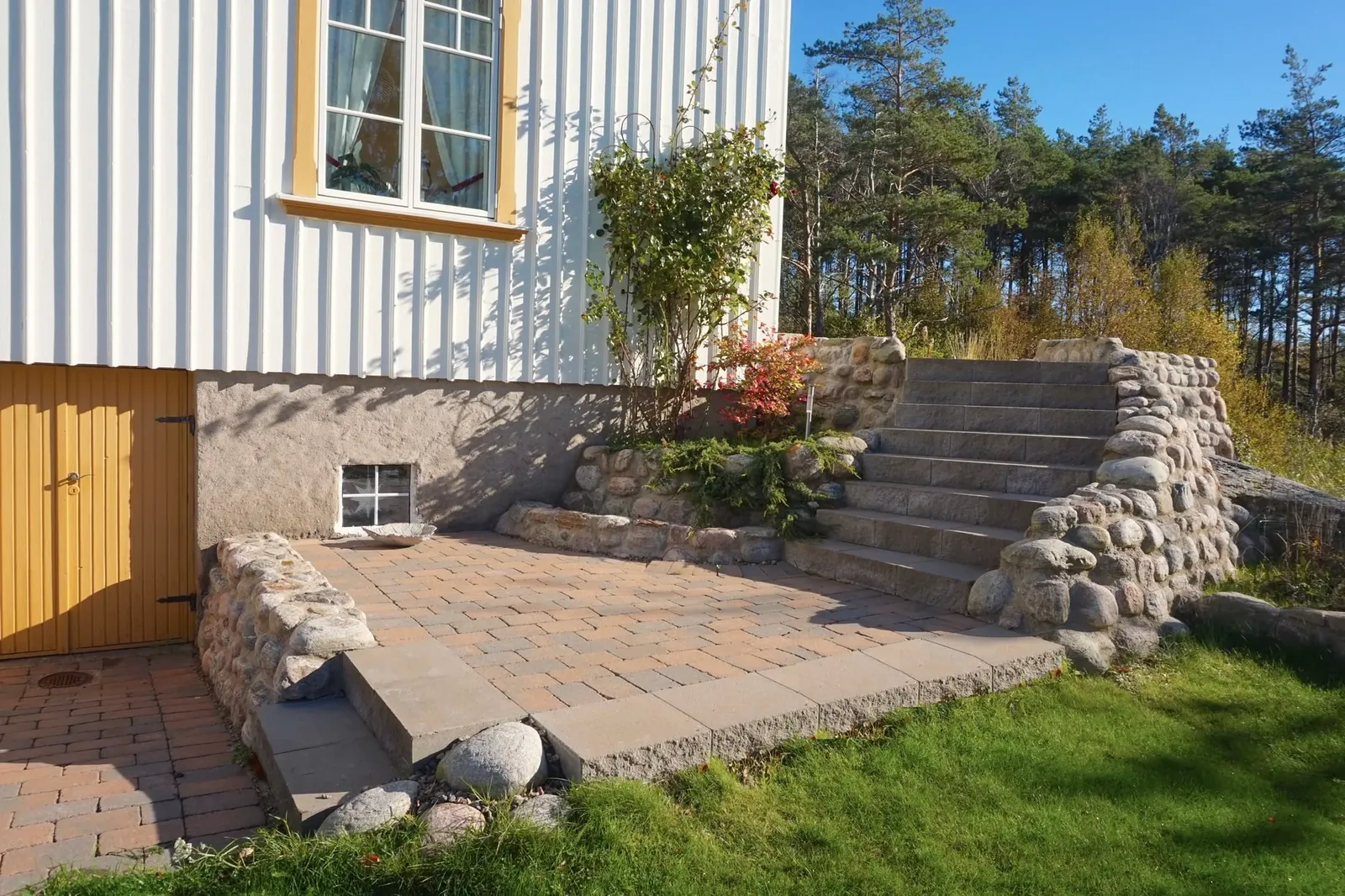 Uteplats och trappa i natursten vid ett hus med gul dörr